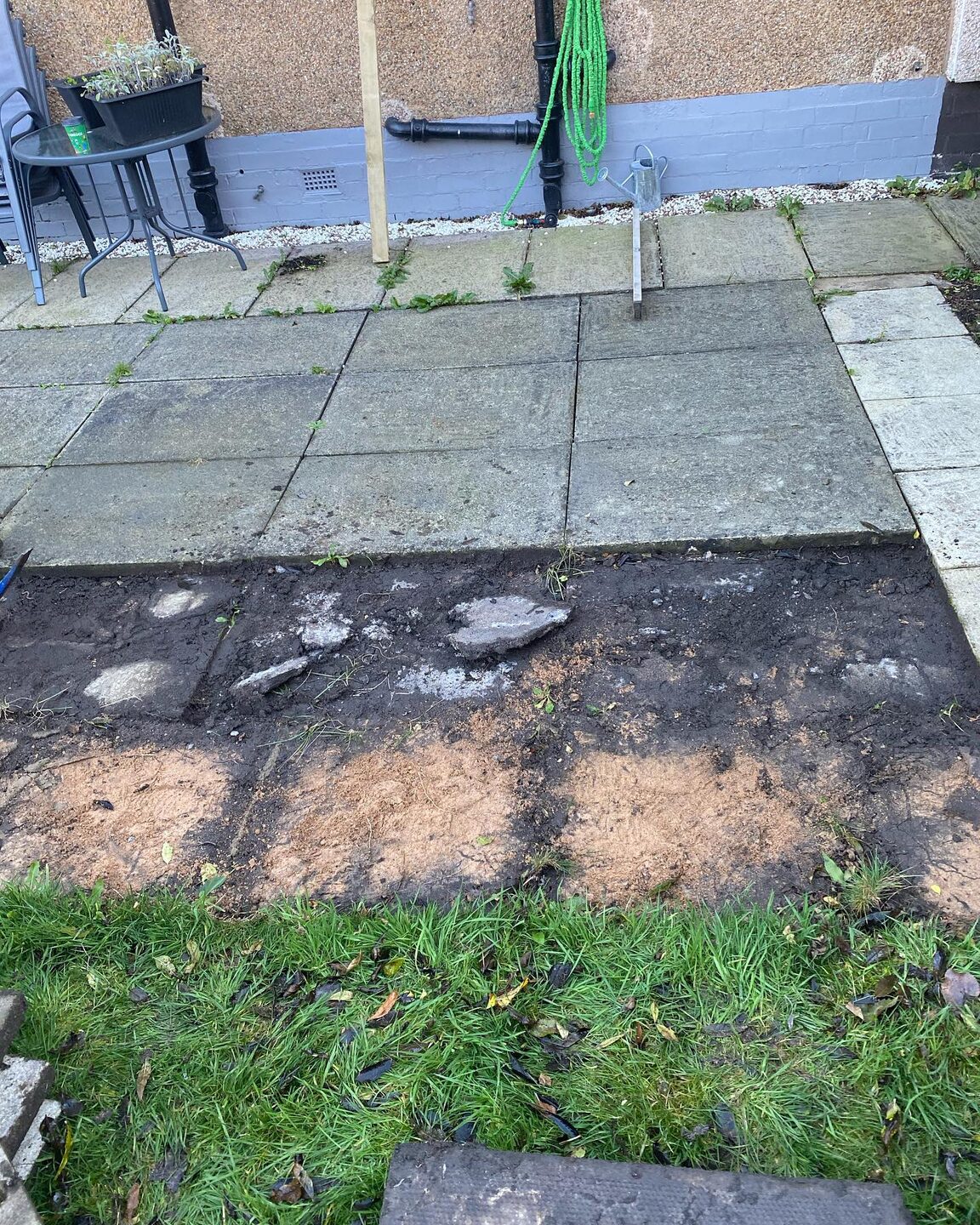 A patio lifted, slabs stacked and the muddy ground underneath exposed
