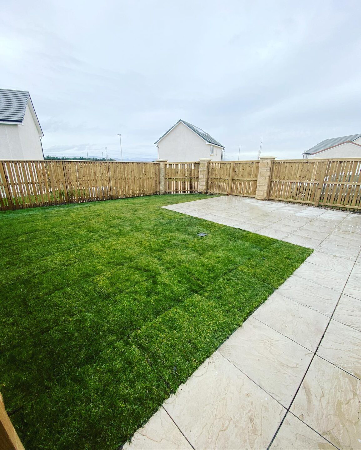 A new-build back garden with fresh green turf and a light slabbed path along the fence